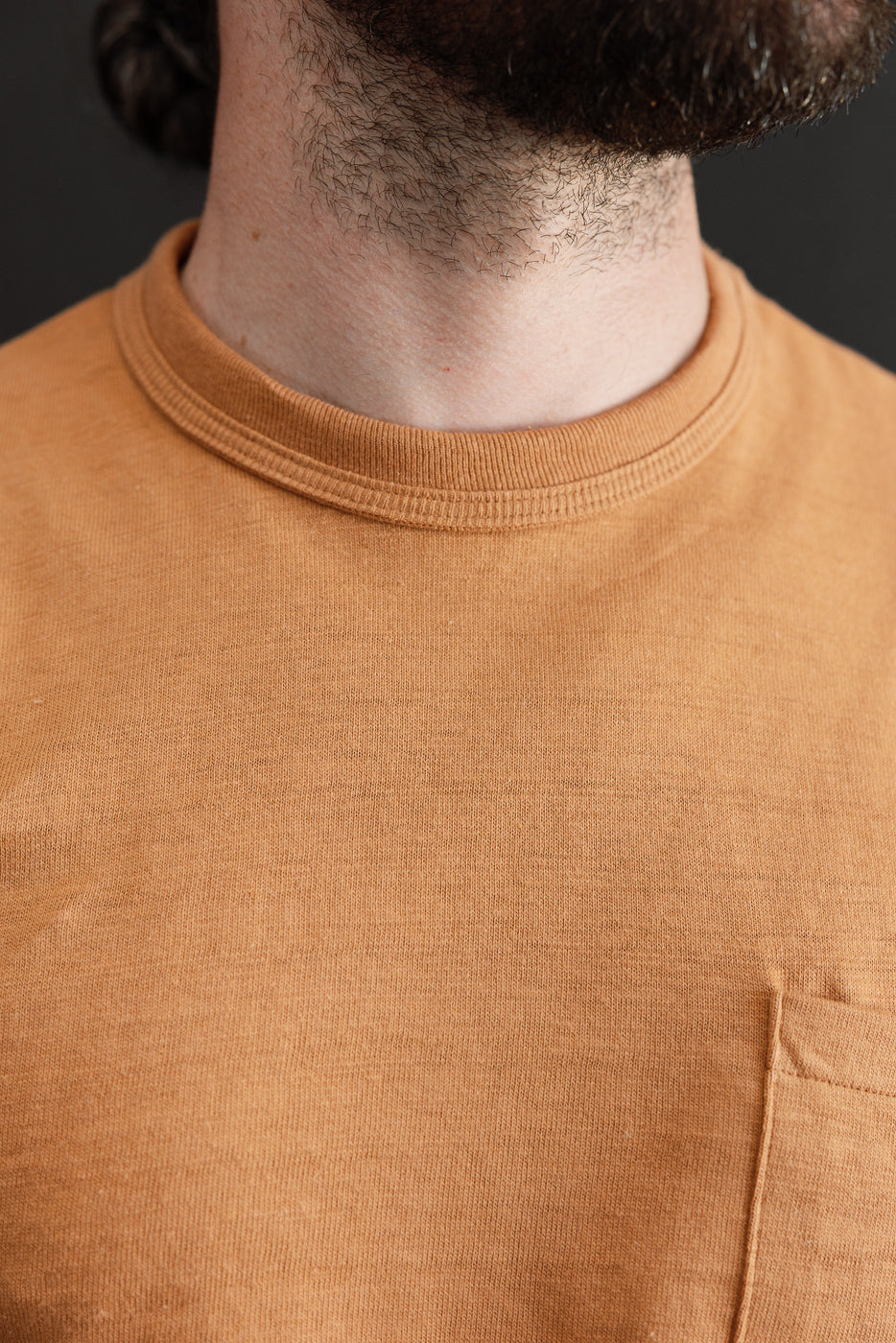Close-up of the front neckline and chest of a tan cotton t-shirt showing ribbed collar texture.