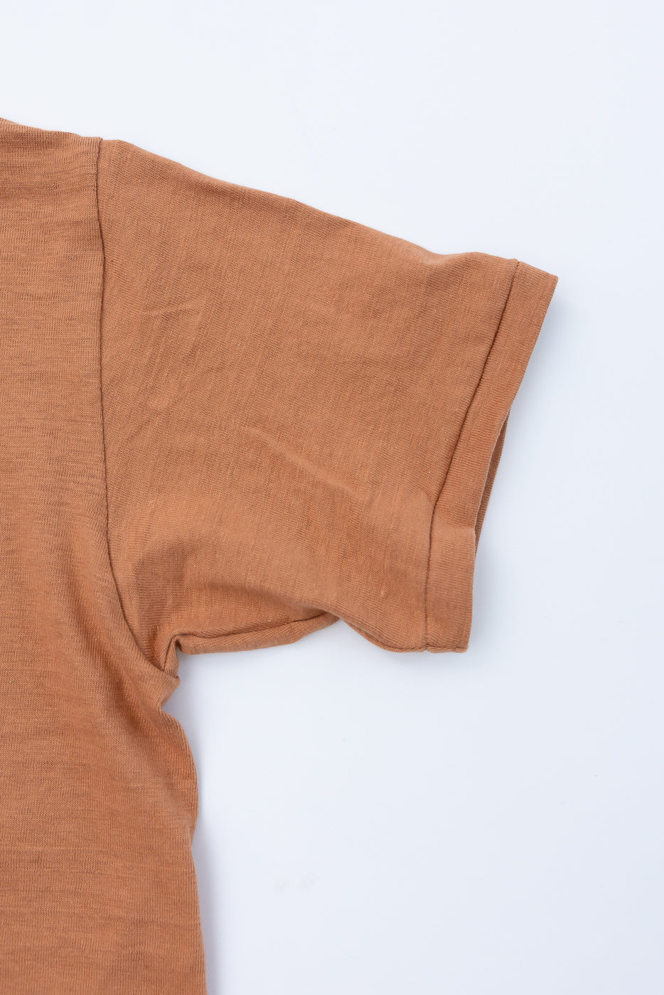 Close-up of the right short sleeve and shoulder seam of a tan cotton t-shirt.