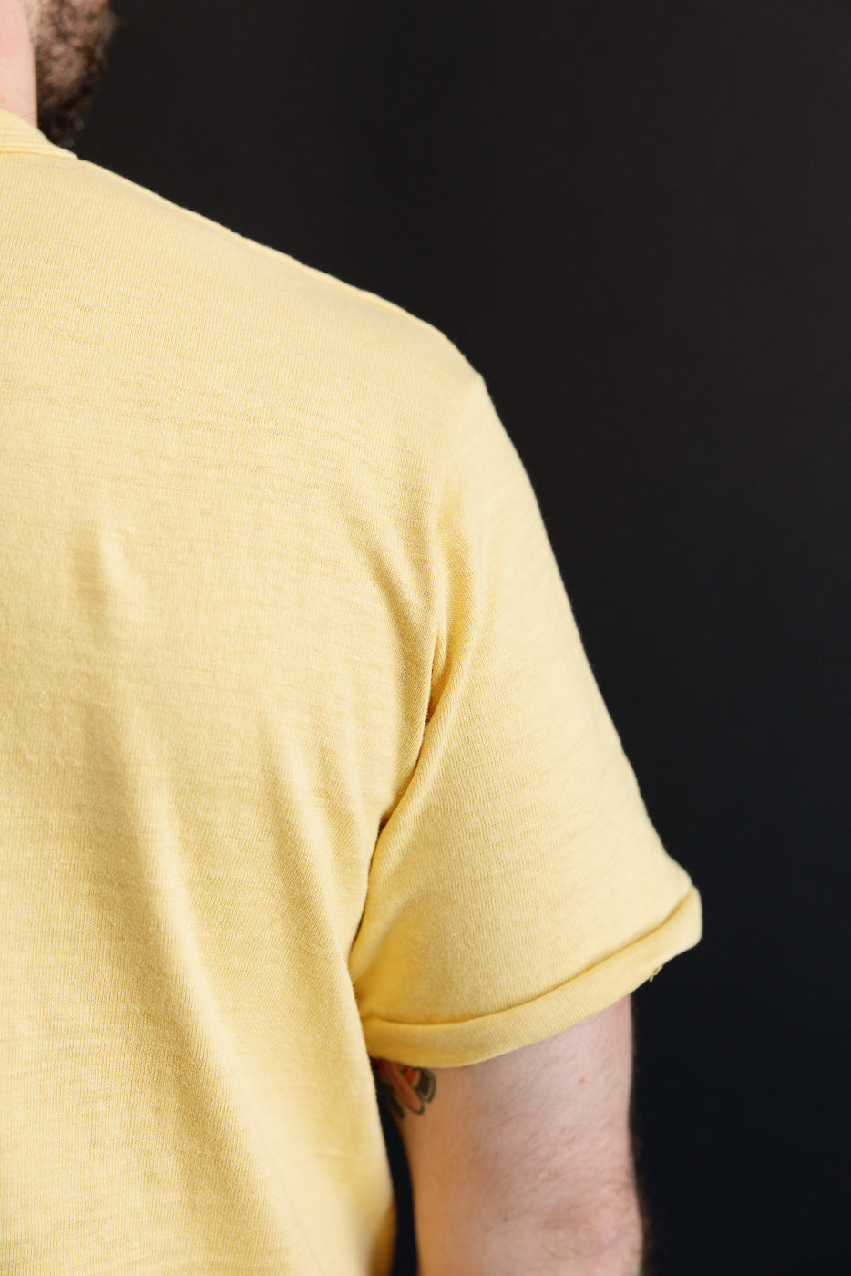 Close-up of the back and rolled sleeve of a yellow cotton t-shirt on a male model.
