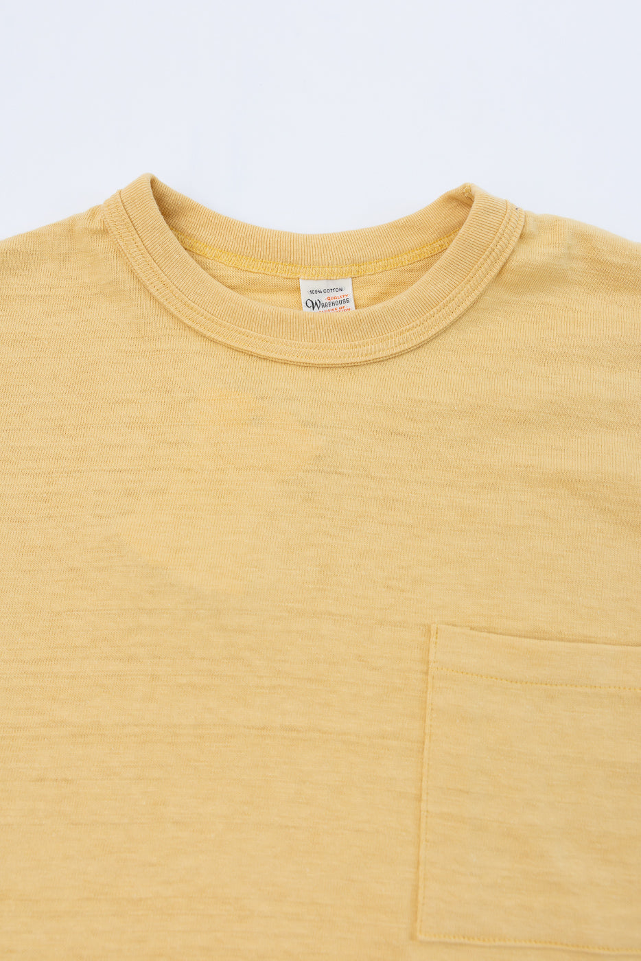 Close-up of the front neckline and chest pocket of a yellow t-shirt with a visible tag.