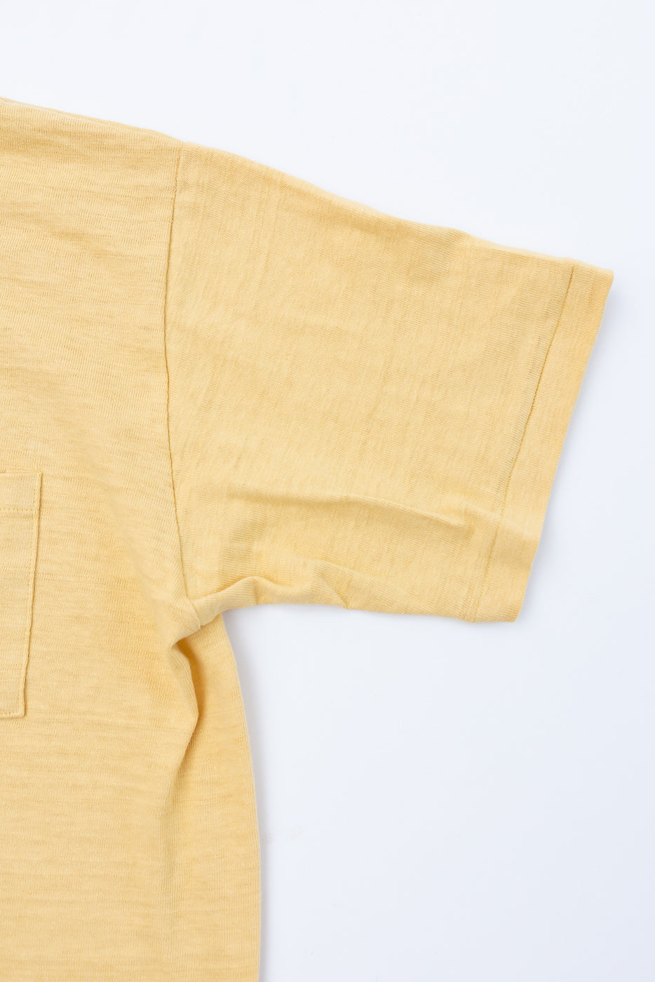 Close-up of the front left sleeve and chest pocket of a yellow textured t-shirt.