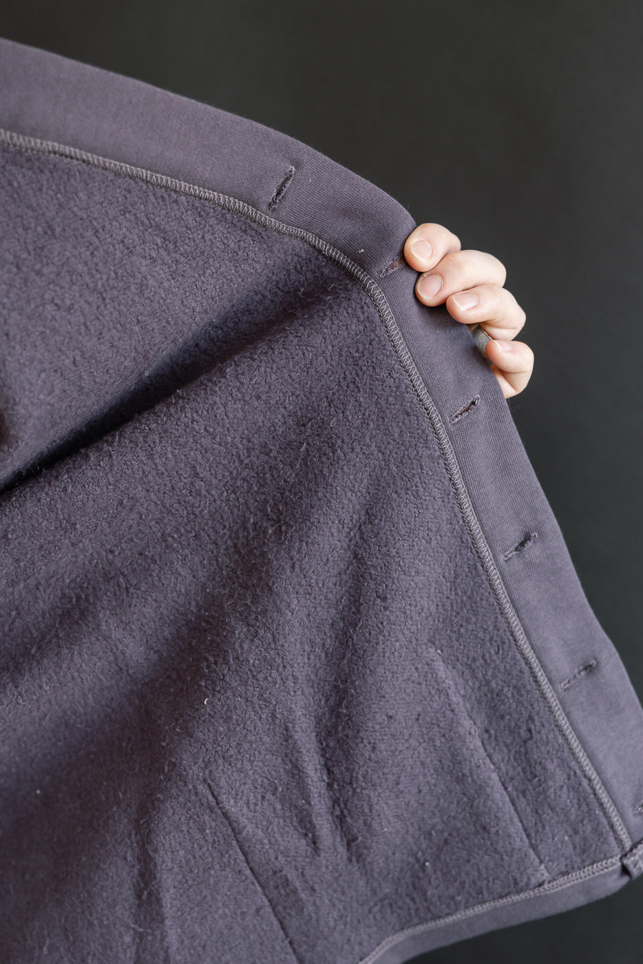 Close-up of dark navy sweat cardigan interior front panel, showing soft fleece texture and buttonholes.