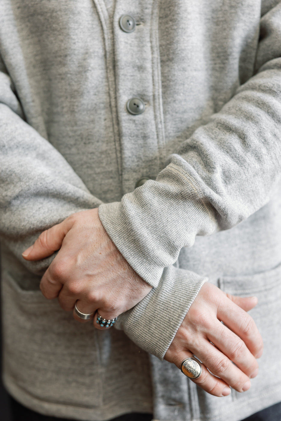 Close-up of male model's hands in heather grey sweat cardigan, showing front buttons and cuff details.