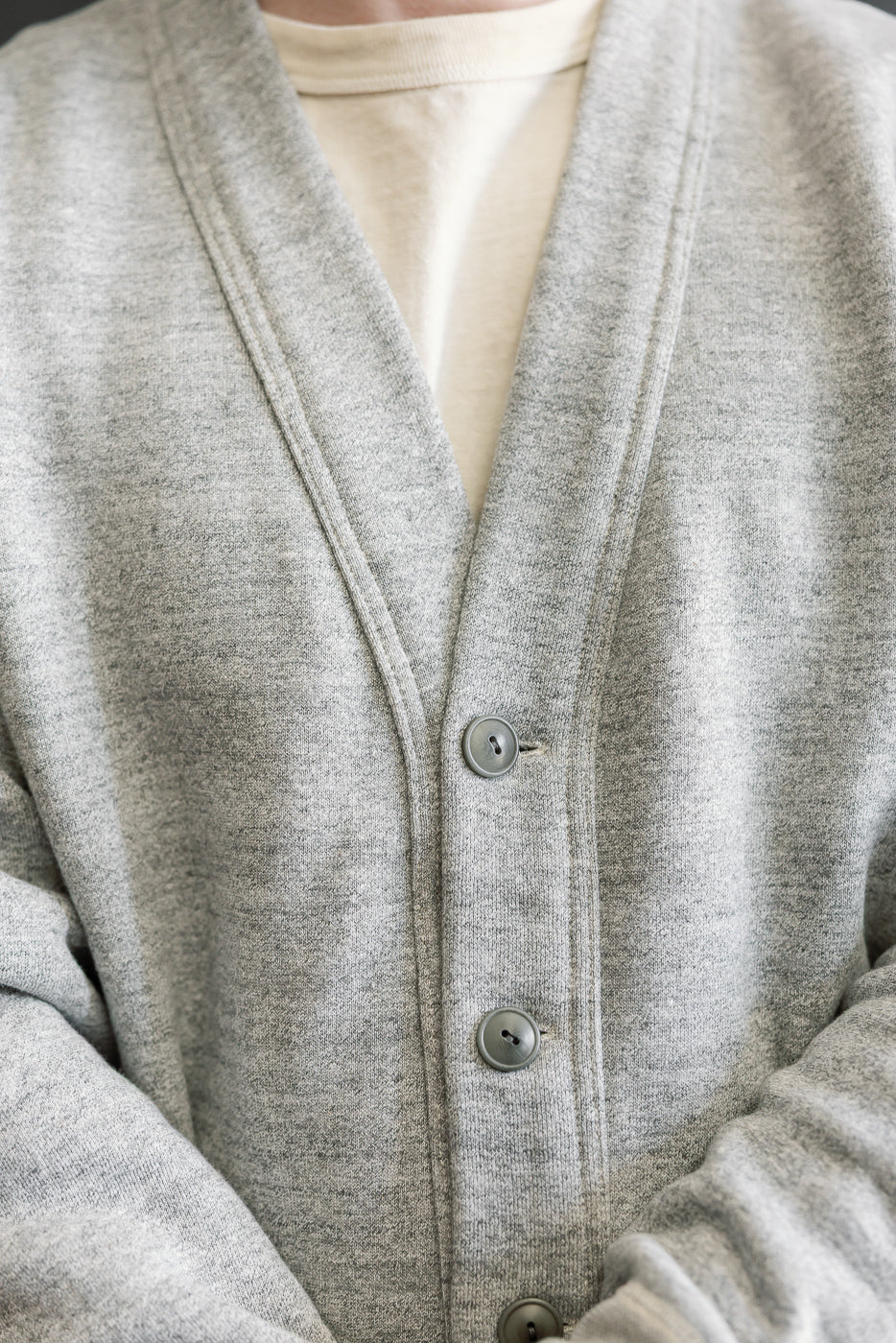 Close-up front view of grey button-up sweat cardigan on male model, showing fabric texture and button details.