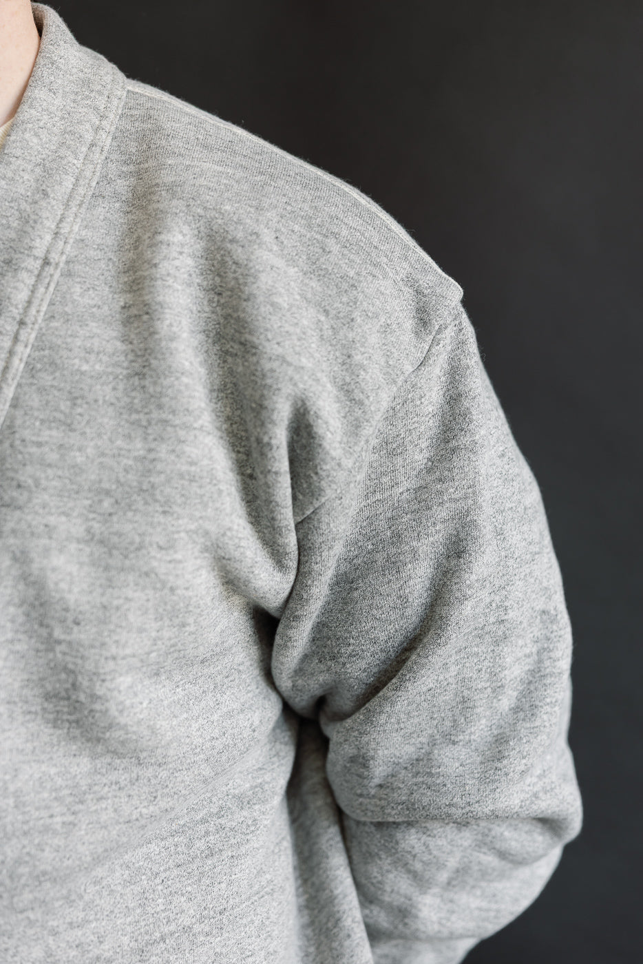 Close-up of heather grey men's cardigan, left shoulder and sleeve, textured fabric detail.