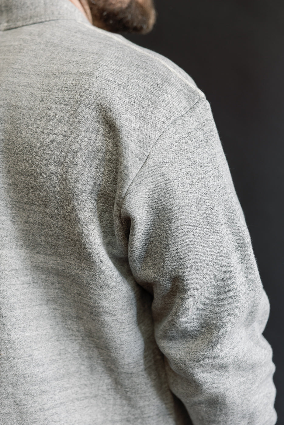 Close-up of the back shoulder and sleeve detail on a heather grey men's sweat cardigan, modeled by a male, showing soft fabric texture.