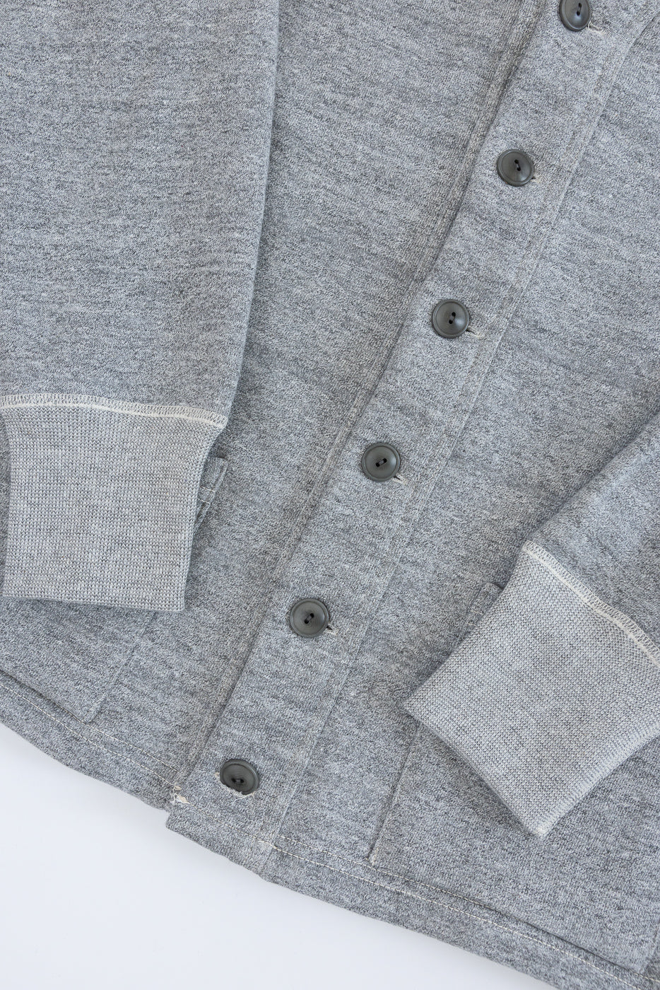 Close-up of heather grey cardigan front, showing button details, knit cuffs, and fabric texture.