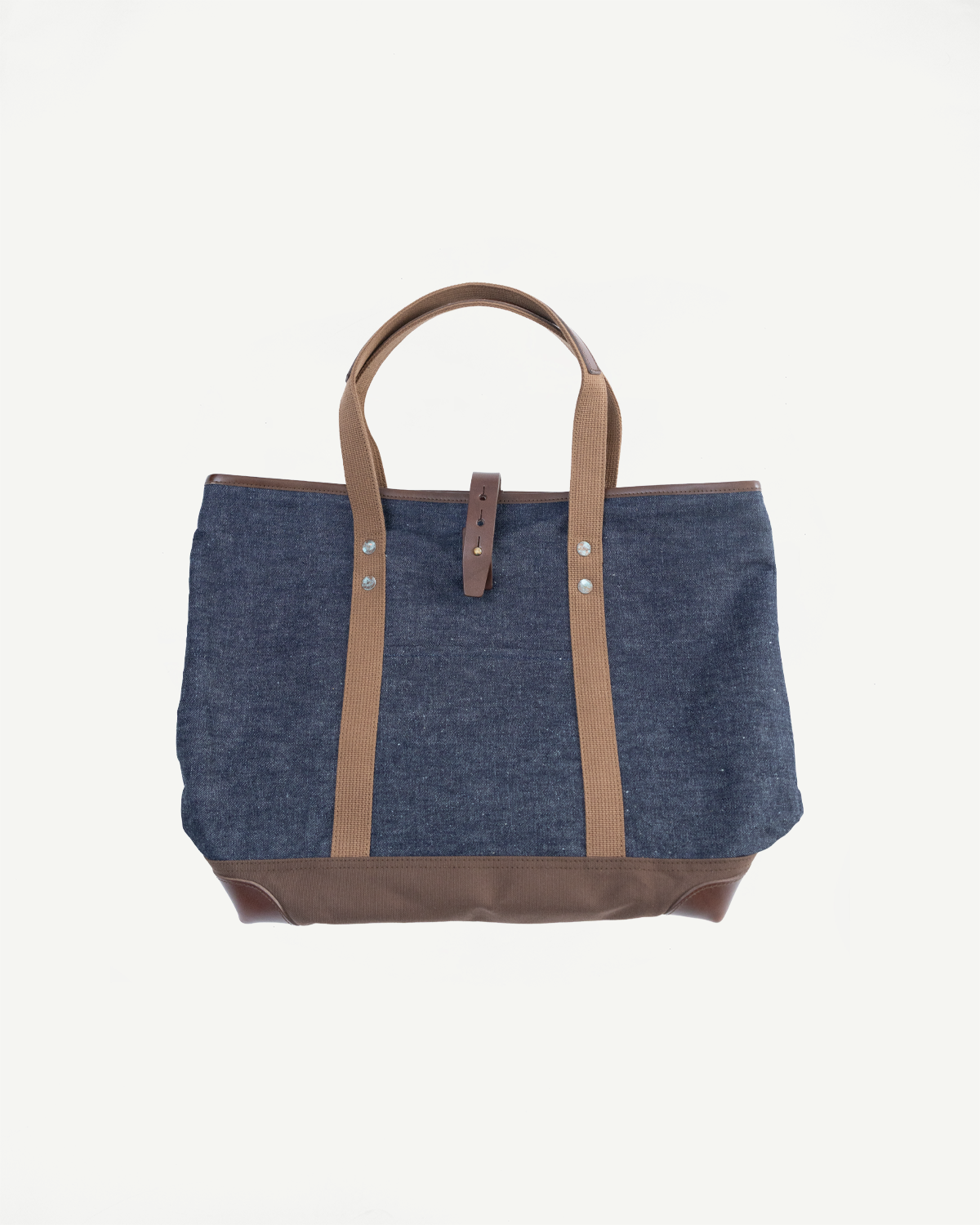 Flat lay front view of indigo denim tote bag with brown handles, rivet details, and leather base