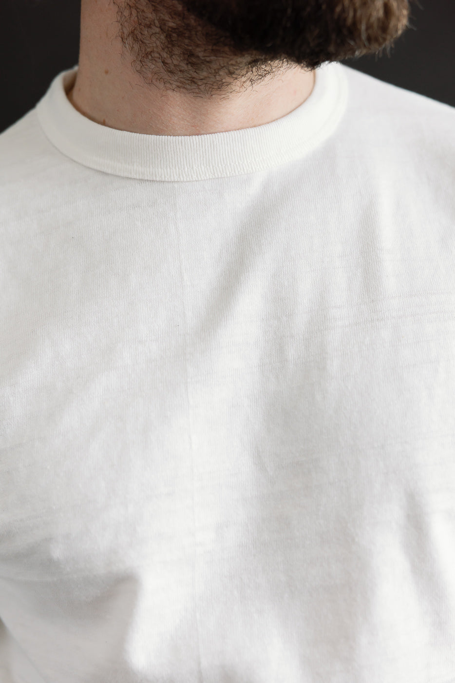 Close-up front detail of Warehouse & Co off-white slubby cotton T-shirt collar and fabric on male model, athletic build, 5'9