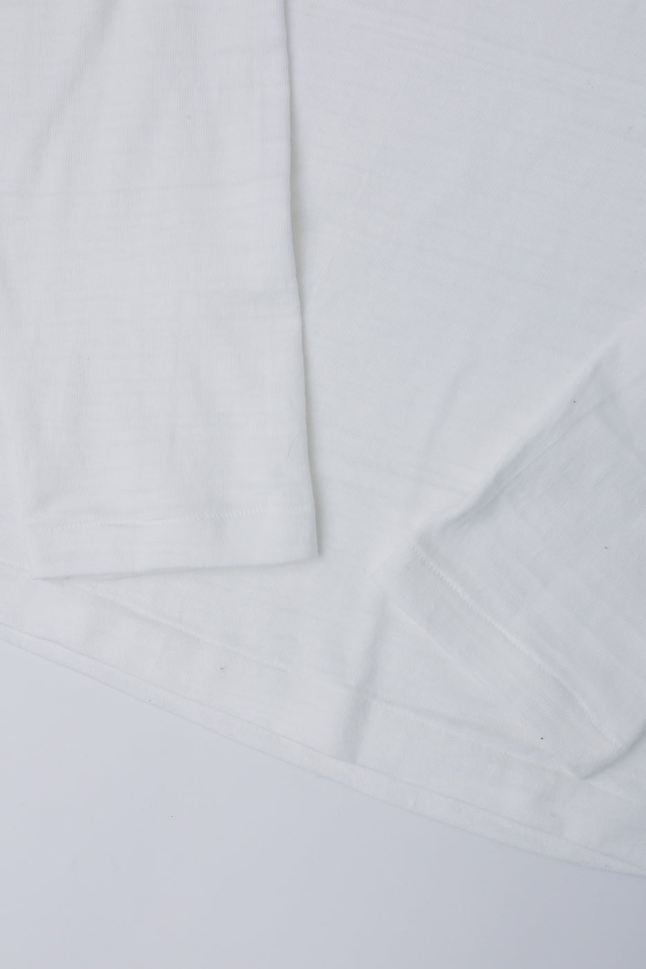 Close-up of Warehouse & Co. off-white slubby cotton long sleeve shirt, flat lay front hem and sleeve, showing fabric texture. Contemporary casual apparel at Dant.