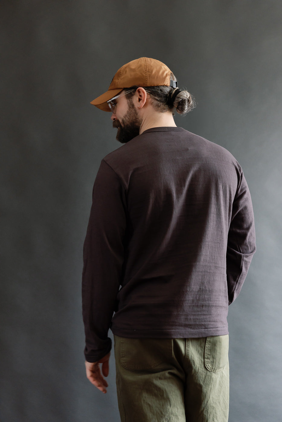 Male model 5'9 165lbs athletic build wearing Warehouse & Co. slubby cotton long sleeve T-shirt in sumi, back view full body, showing rear fit and fabric texture.