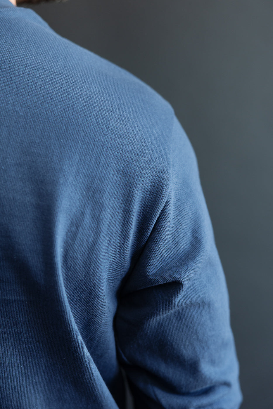 Close-up of the back and right sleeve of a blue textured long-sleeve shirt.