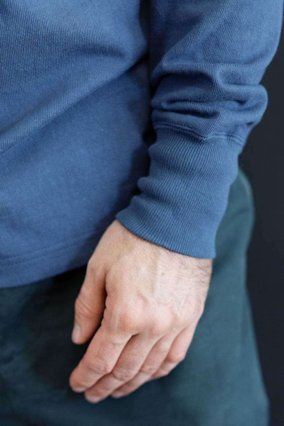 Close-up of the cuff and sleeve of a male model's blue long-sleeve sweatshirt.