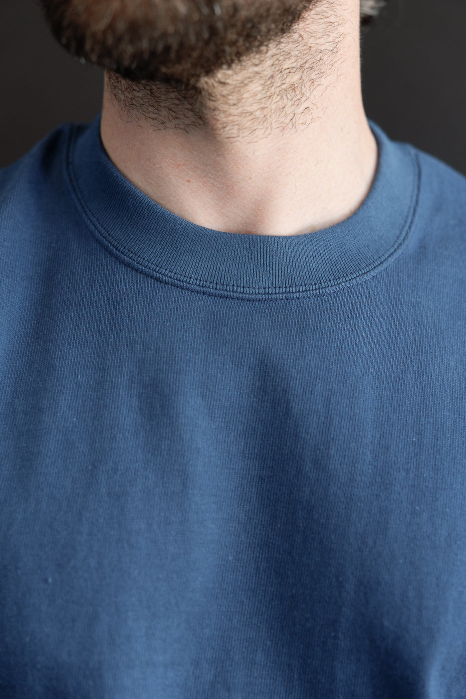 Close-up of the front ribbed crewneck collar and fine cotton texture of a blue sweatshirt.