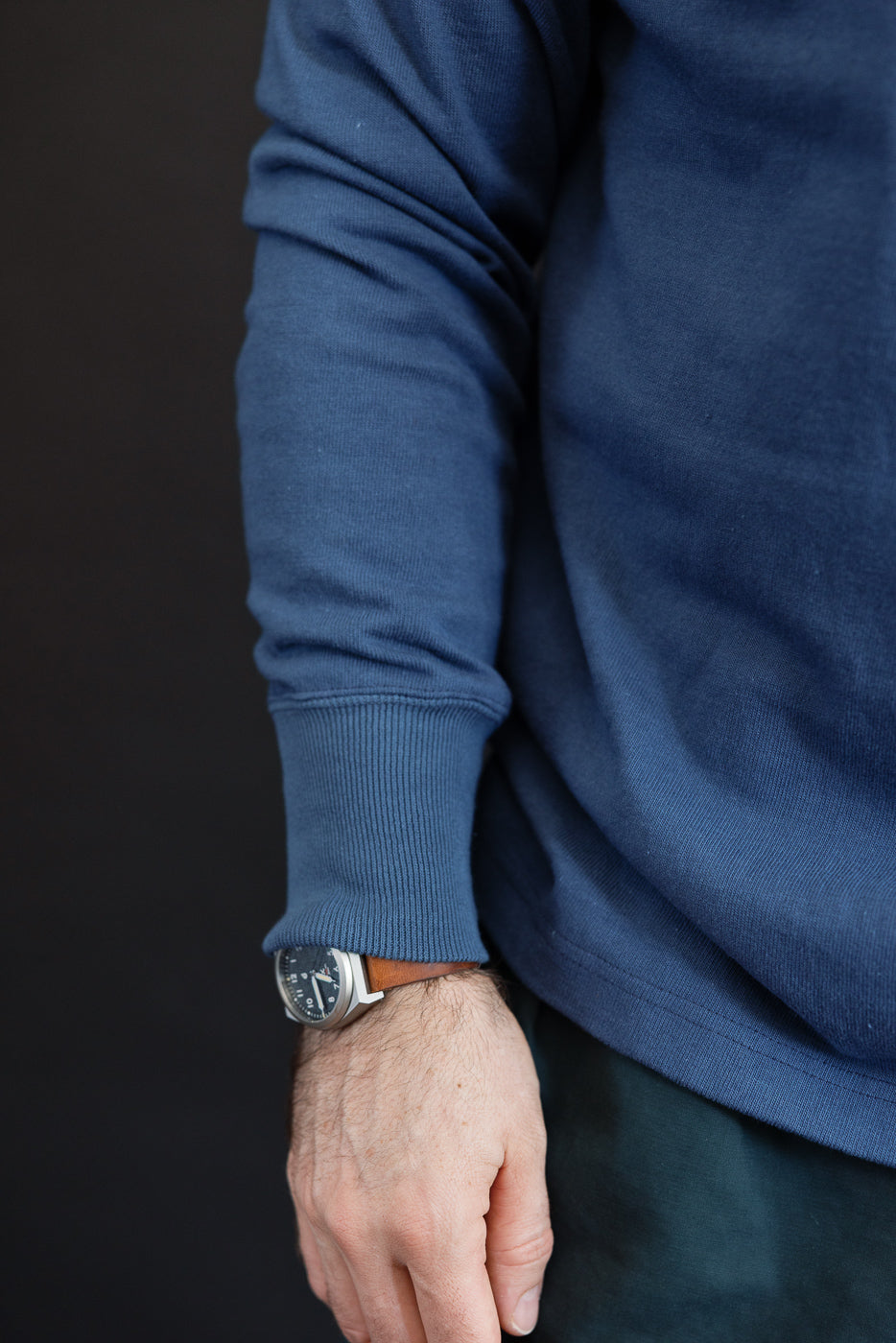 Close-up of the left sleeve and cuff of a blue long-sleeve sweatshirt worn by a male model.