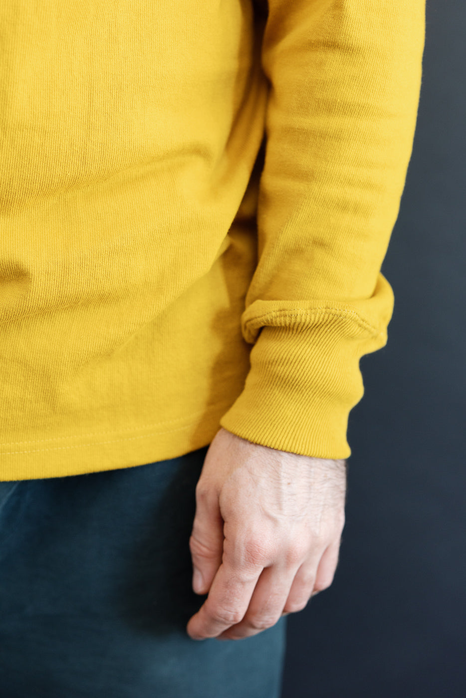 Close-up of the side and ribbed cuff of a yellow long-sleeve shirt worn by a male model.