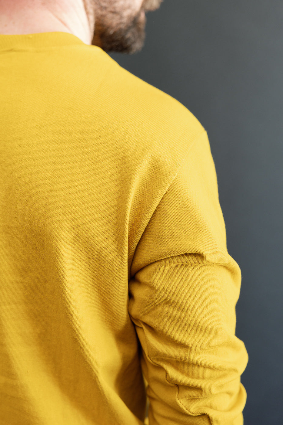 Close-up view of the back and right sleeve of a mustard yellow long-sleeve textured cotton shirt.