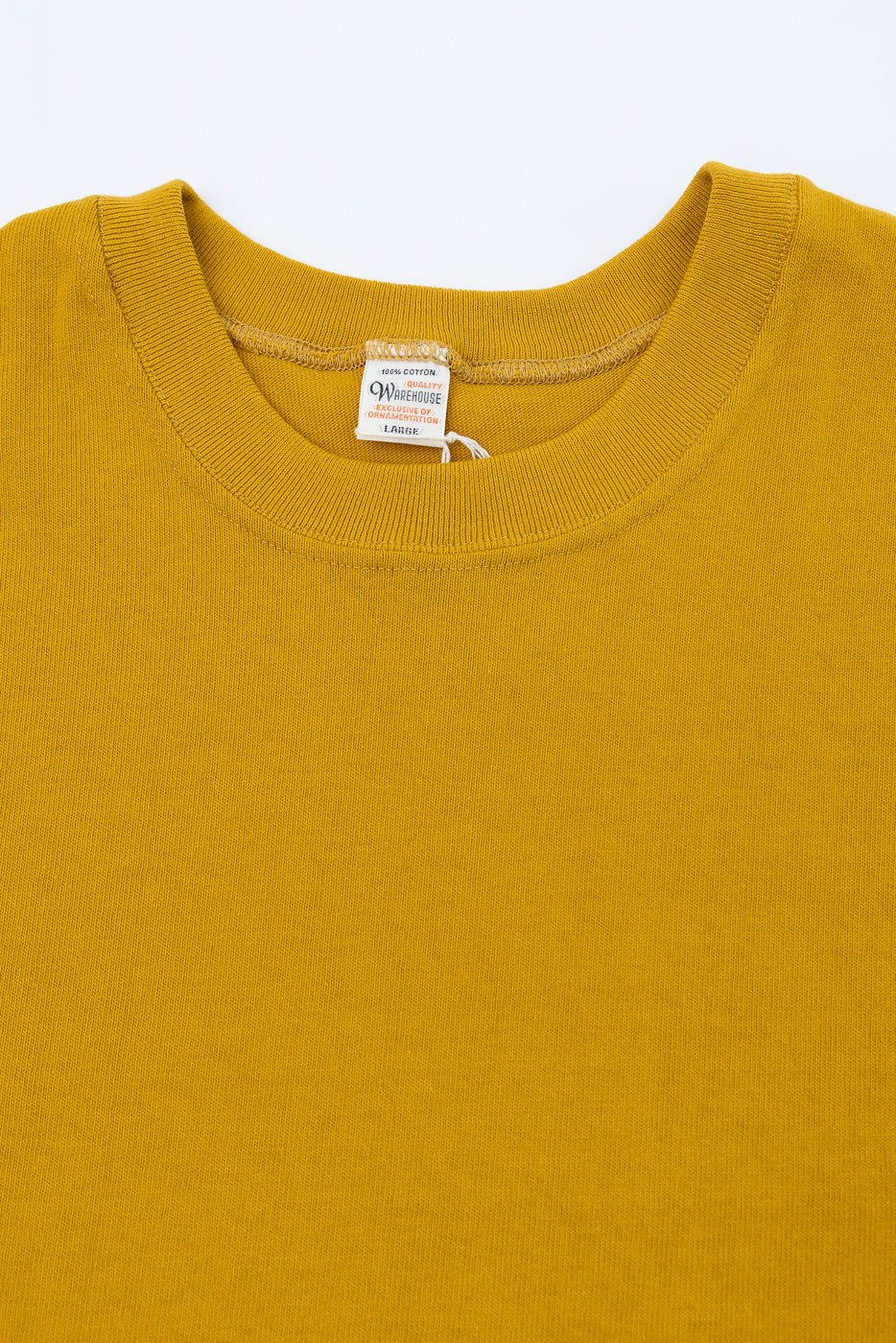 Close-up front view of the crew neck collar and white brand tag on a mustard yellow cotton t-shirt.