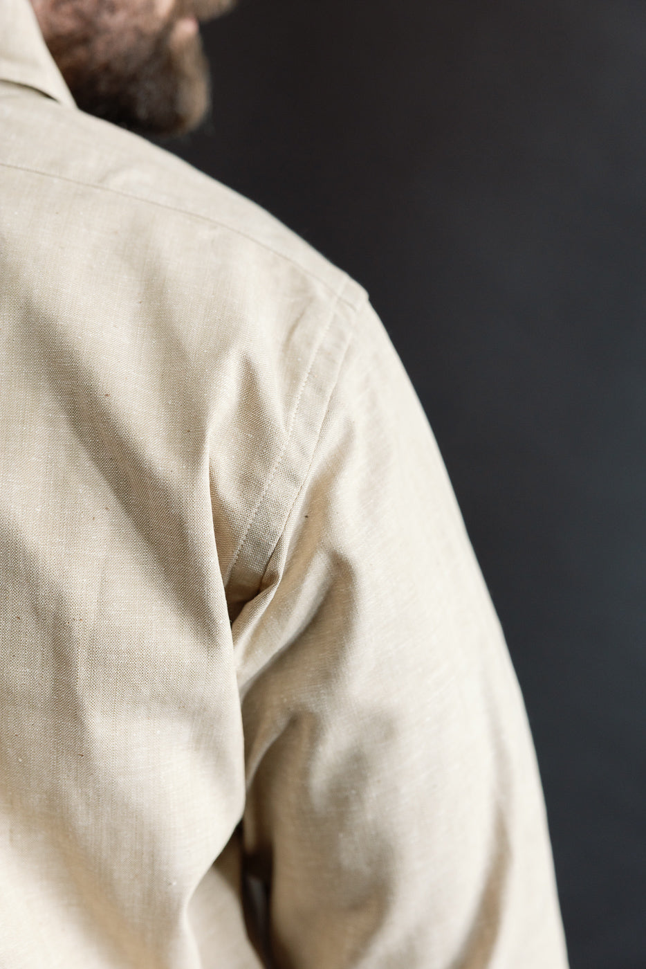 Close-up of male model’s left shoulder and upper back in brown oxford shirt, fabric texture visible, athletic build, partial profile view.