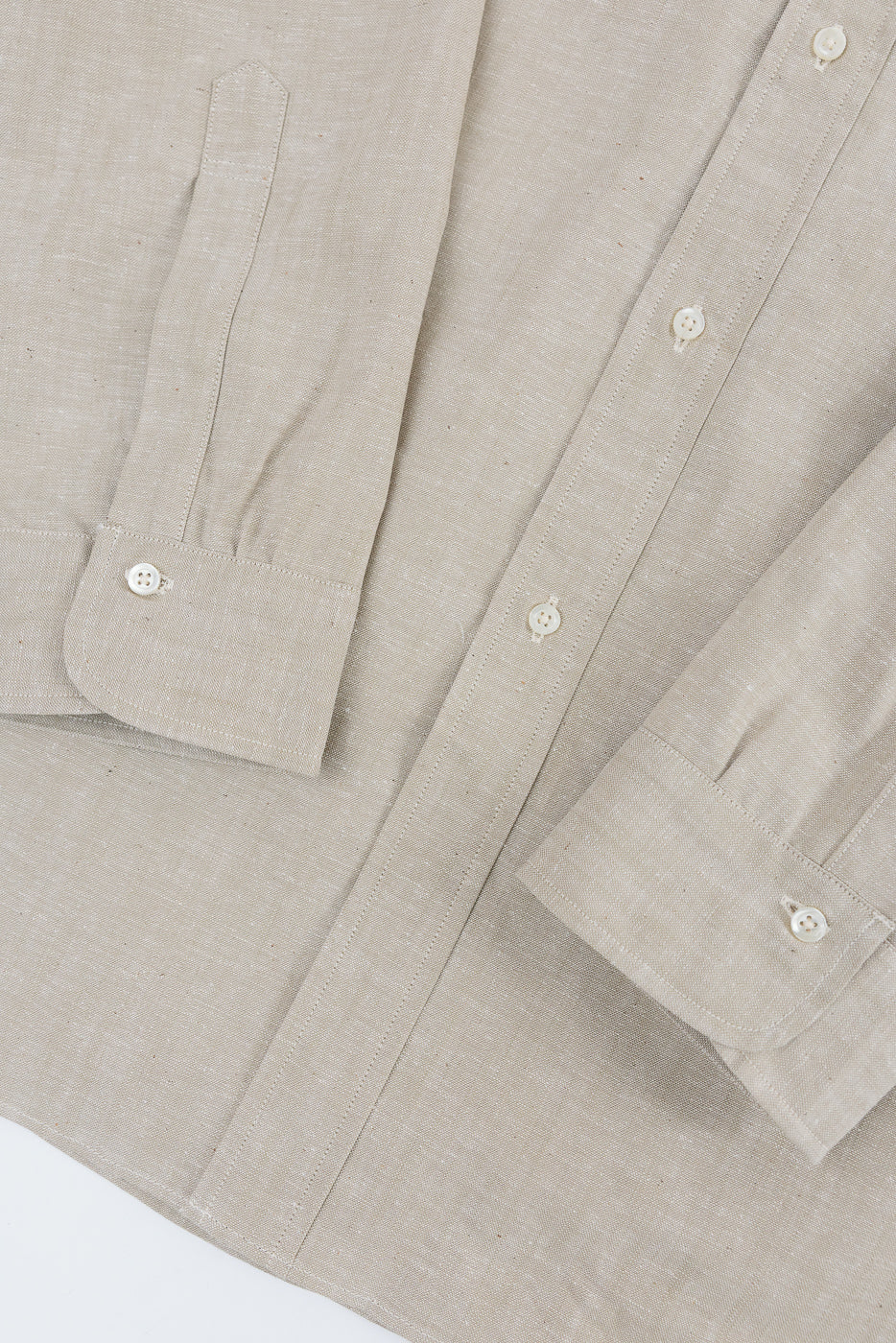 Close-up of oxford shirt front, showing sleeve cuffs, placket, and beige fabric texture.