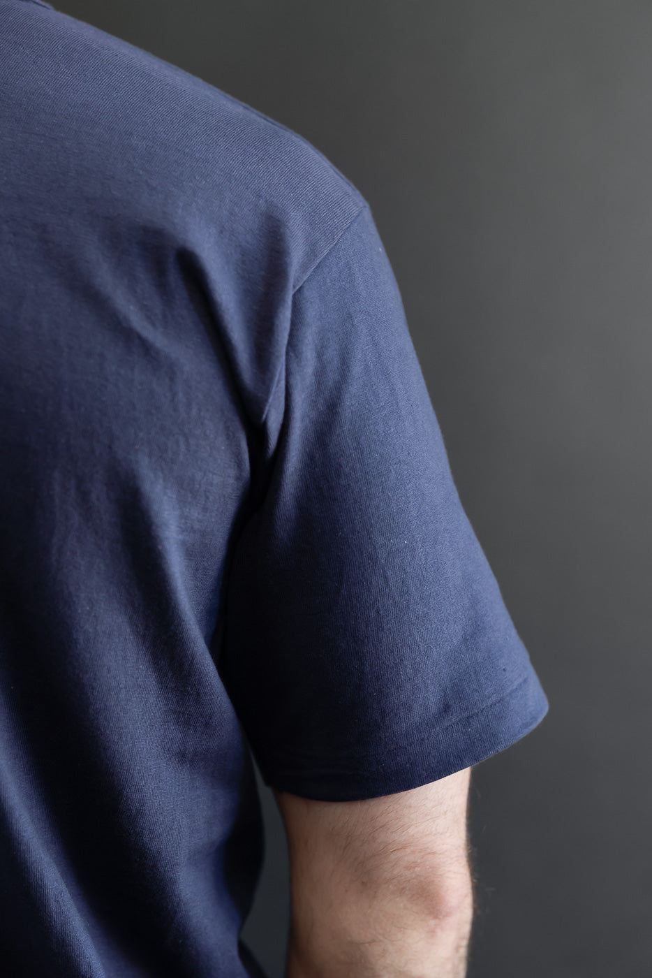 Close-up of the back and sleeve of a navy blue t-shirt on a male model, 5'9