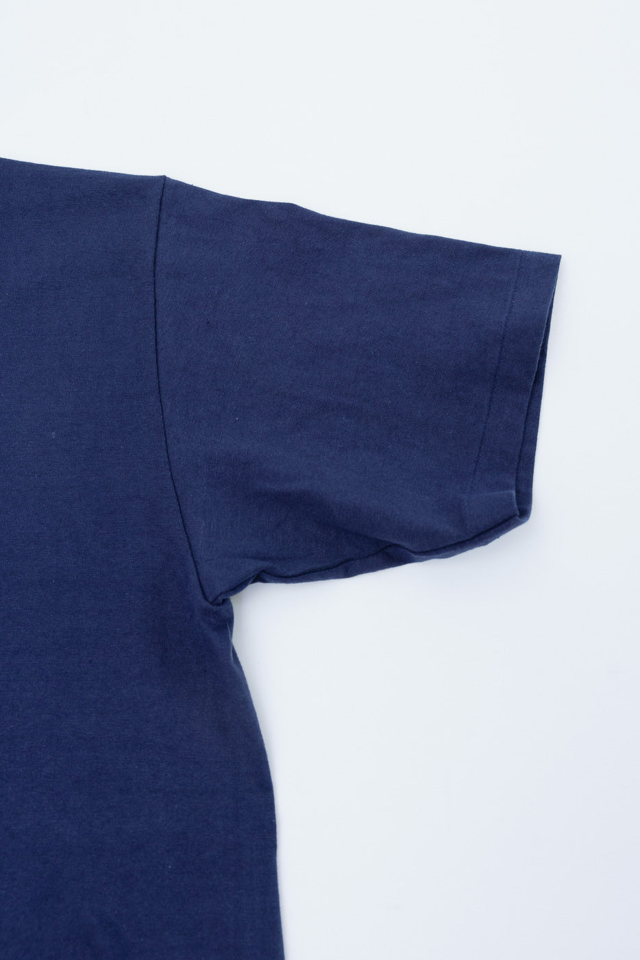 Close-up of the left sleeve and side of a navy blue cotton t-shirt flat lay.