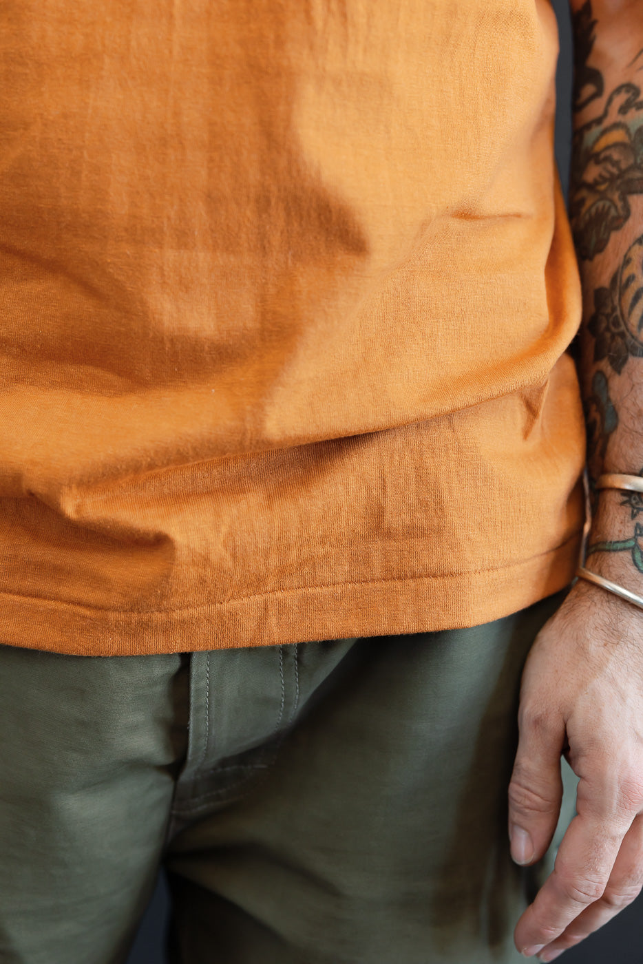 Close-up of the front hem of an orange t-shirt on a male model, 5'9