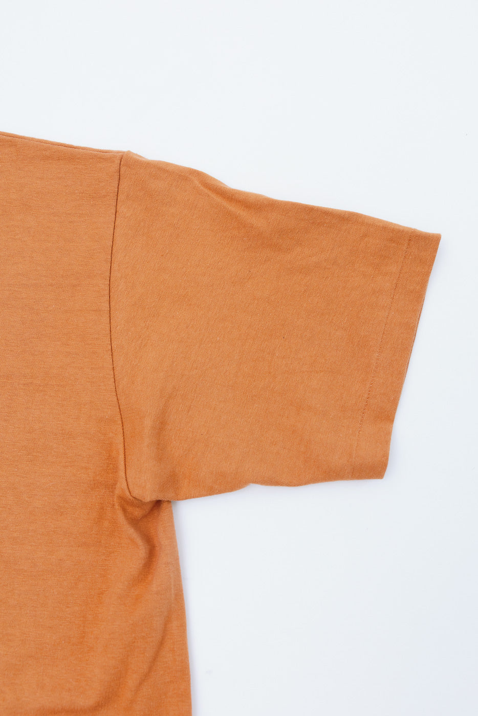 Close-up of the right sleeve and side of an orange t-shirt flat lay, showing fabric texture.