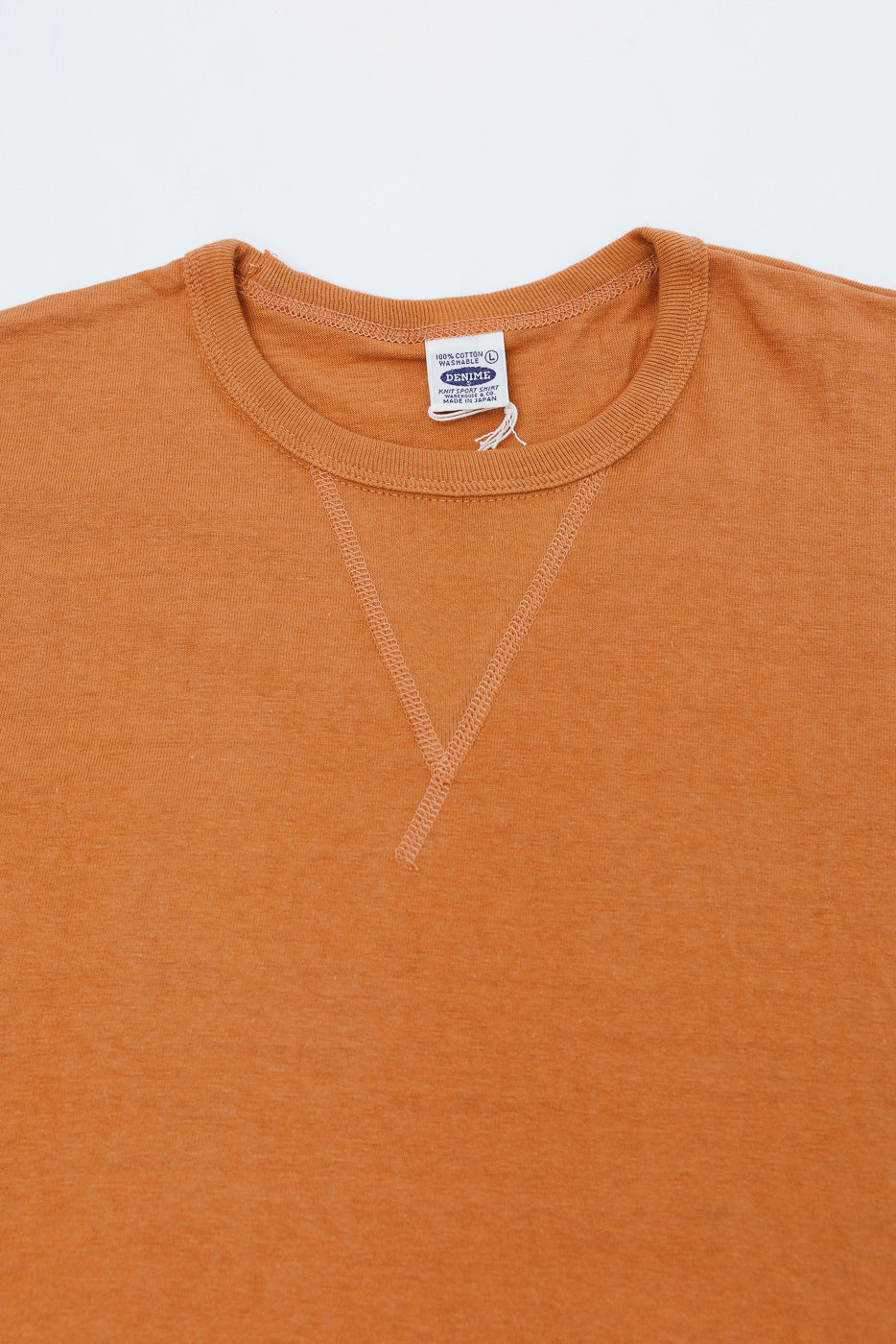 Close-up of the front collar and neckline of an orange t-shirt showing the Denime brand tag.