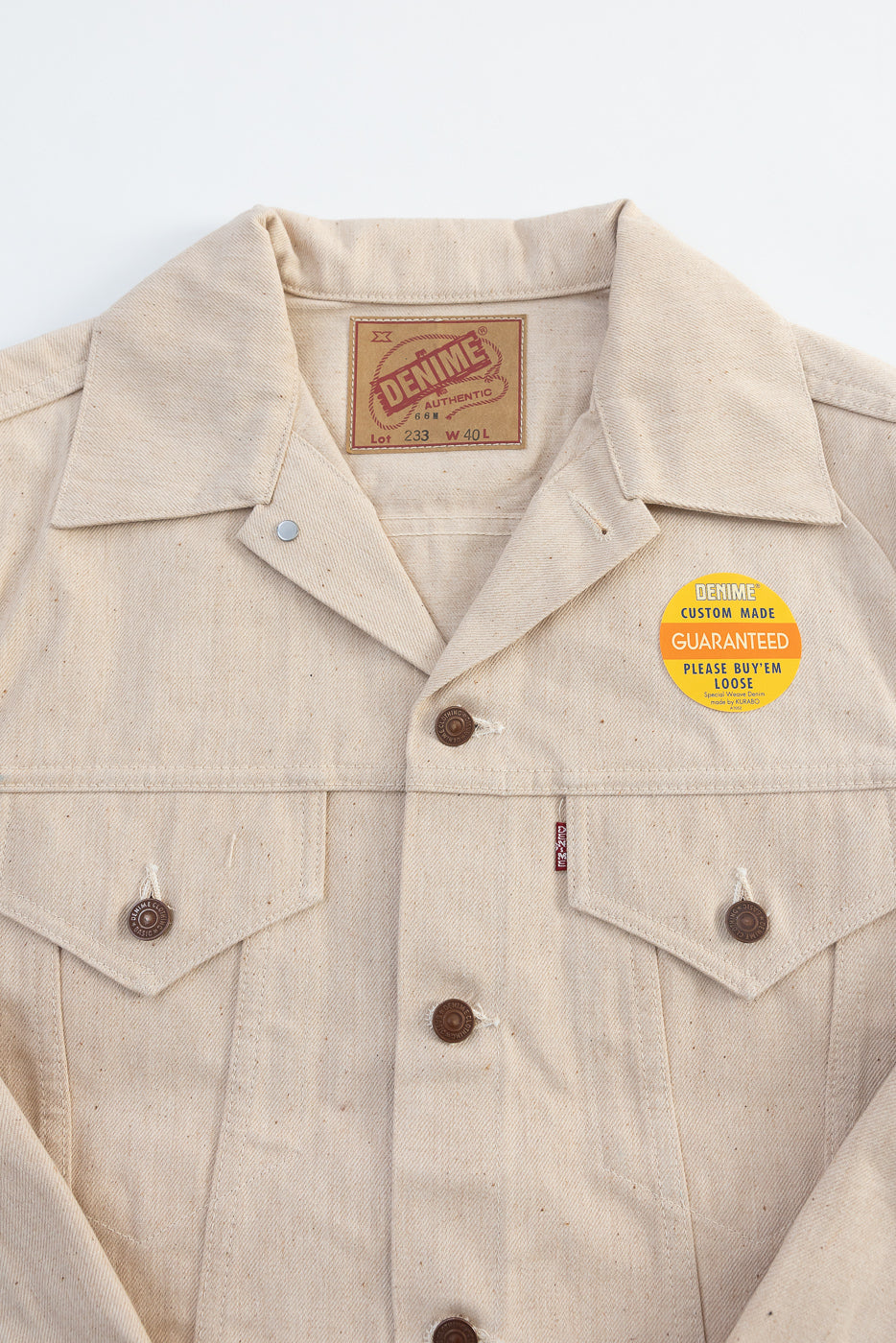 Close-up front view of Denime Lot 66M ecru cotton jacket showing collar, buttons, chest pockets, and tag.