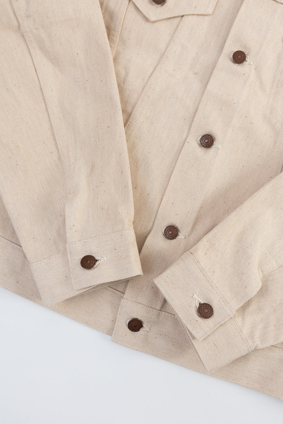 Close-up of front hem and sleeve cuffs of ecru Warehouse Denime Lot 66M 3rd Type Jacket, showing brown buttons, sturdy cotton fabric, and precise stitching.