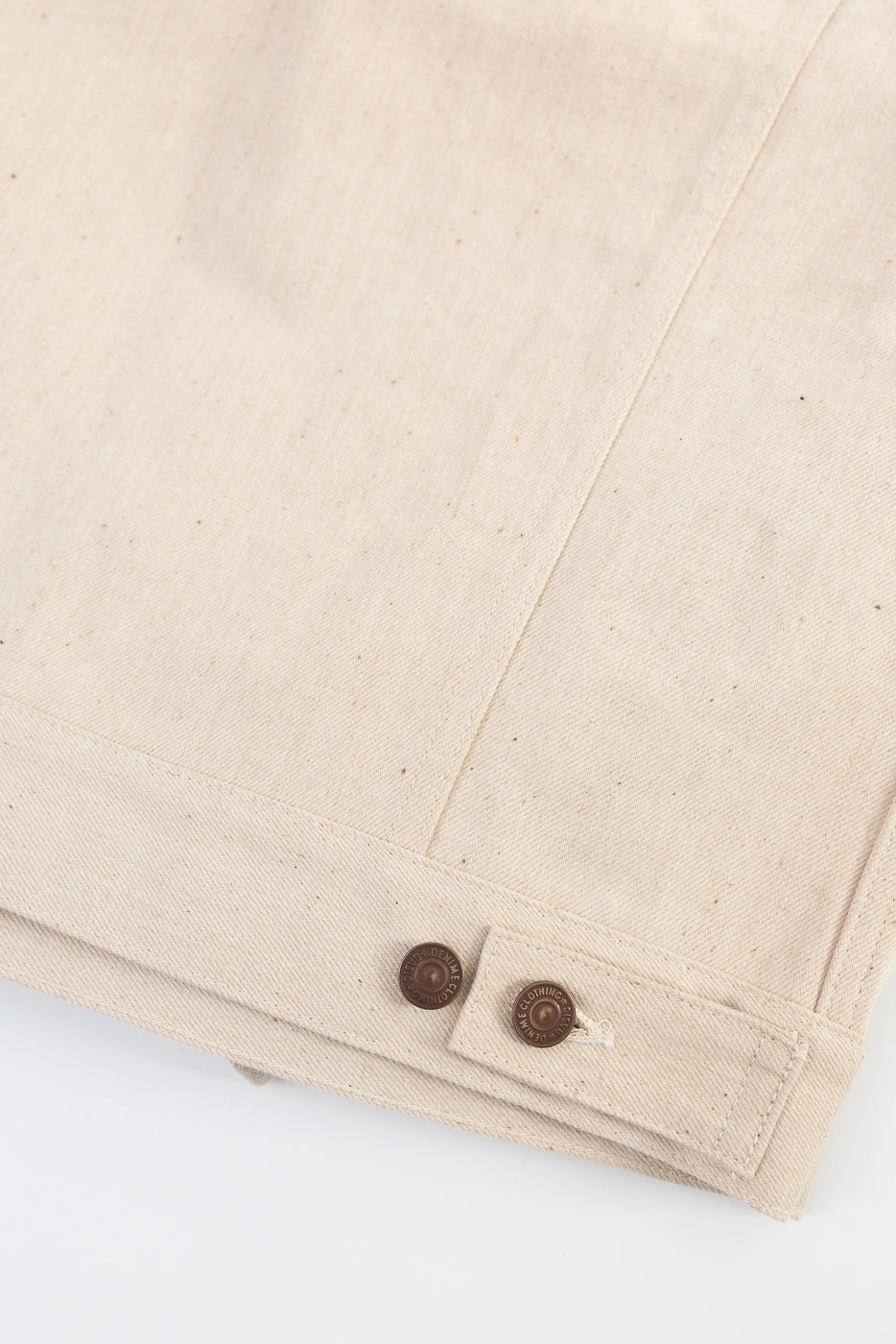 Close-up of Warehouse Denime Lot 66M ecru denim jacket hem and brown button details, back side.