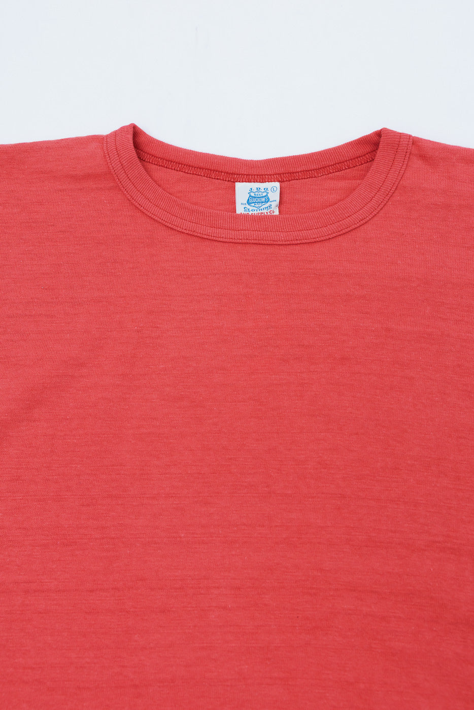 Close-up of the front crew neck collar and white brand tag on a red textured cotton t-shirt.