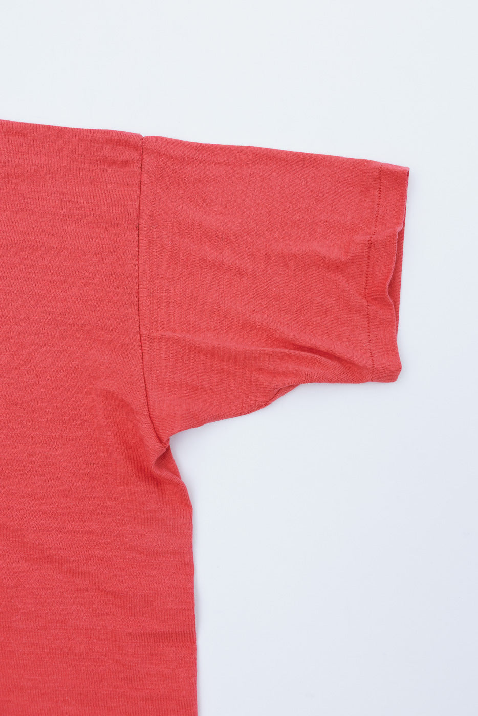Close-up of the right short sleeve and shoulder seam of a red cotton t-shirt.