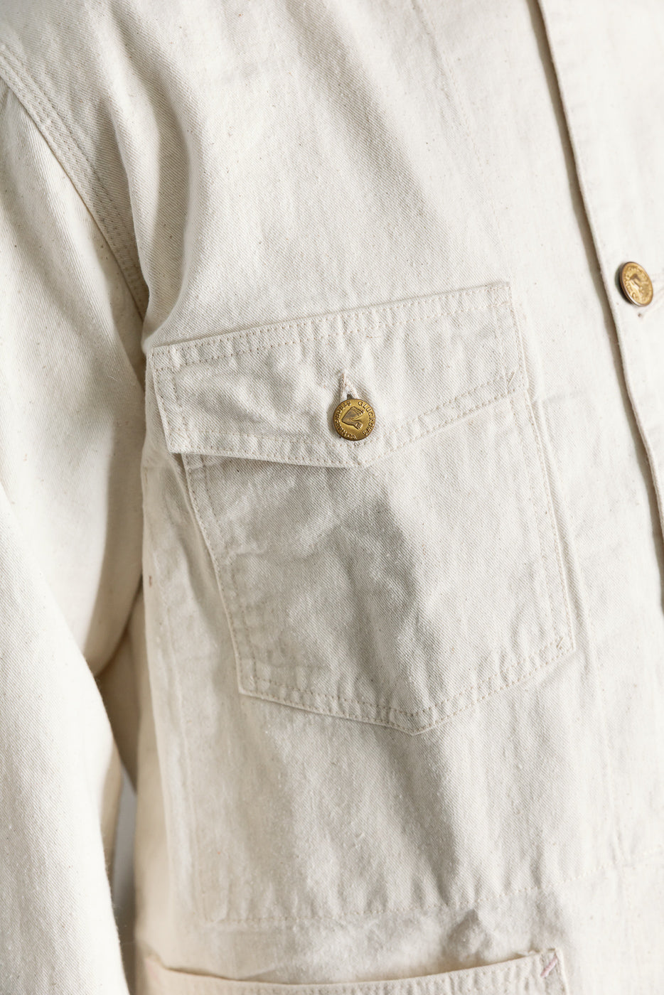 Close-up of ecru canvas painters jacket front chest pocket with gold button details, Dant