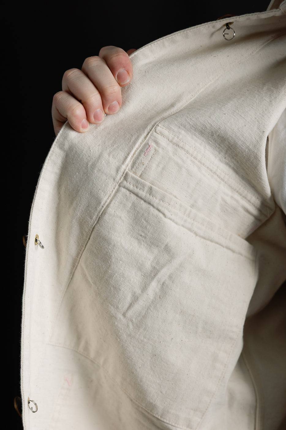 Close-up of inside front left panel of ecru house painter's jacket showing interior pocket and textured selvedge fabric details.