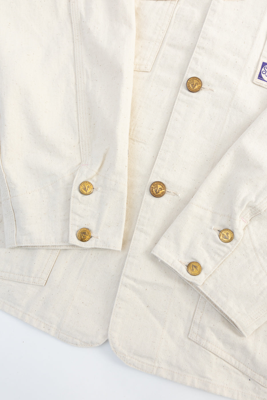 Close-up of front ecru house painter's jacket cuffs showing brass buttons and canvas texture