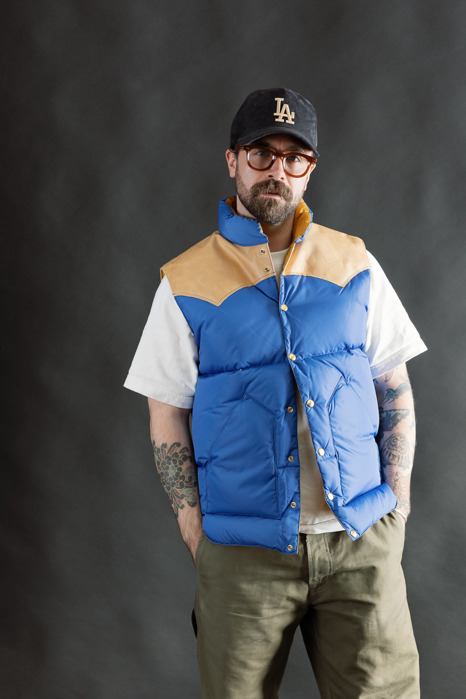 Front view, male model 5'9 165lbs athletic build in blue Rocky Mountain nylon down vest, snap buttons, tan yoke, Dant casual apparel