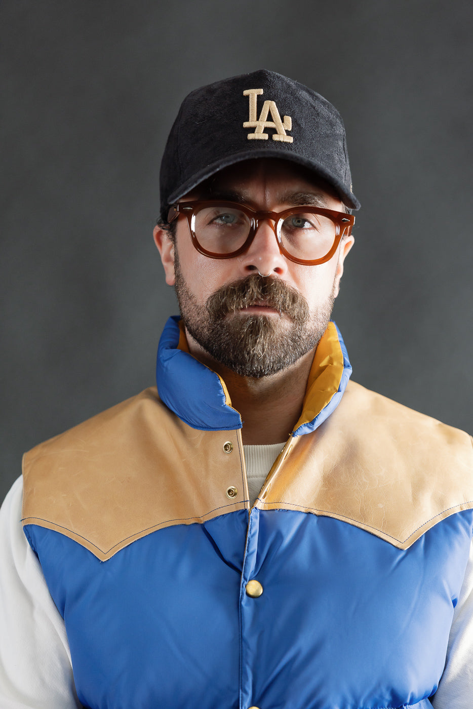 Close-up front of blue nylon down vest with tan yoke, worn by male model 5'9 165lbs athletic build