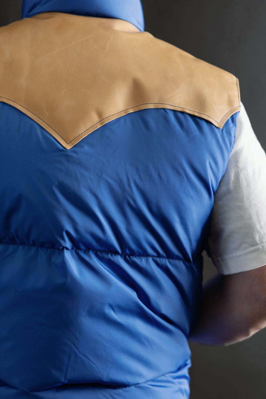 Close-up back view of blue Rocky Mountain nylon down vest with tan yoke on male model, 5'9