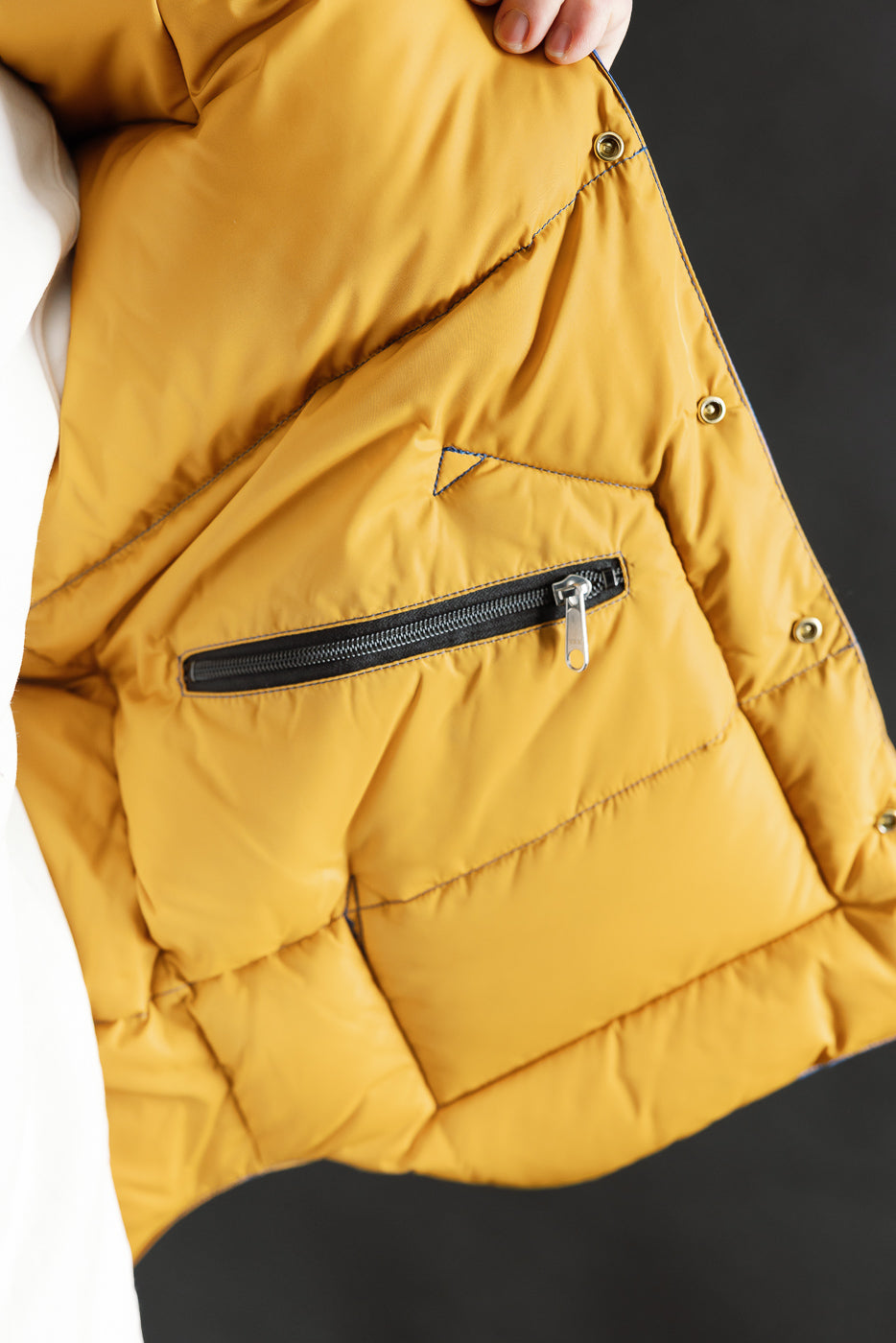 Close-up of inside front left of Rocky Mountain Warehouse yellow nylon down vest, showing inner zip pocket and snap buttons.