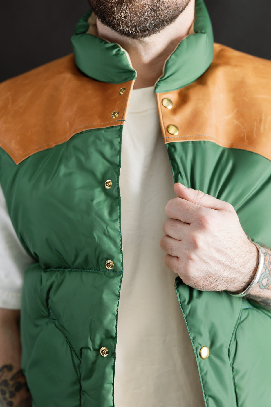 Close-up front view of bottle green nylon down vest with tan yoke, snap buttons; male model 5'9