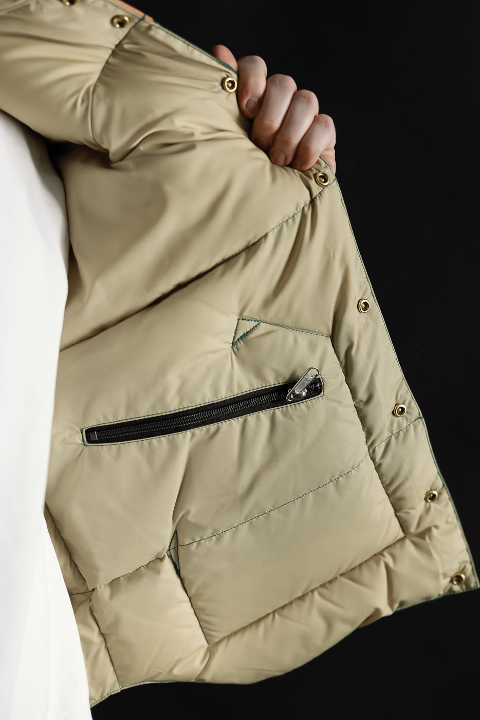 Close-up of men's nylon down vest interior, beige lining, zipper pocket, snap buttons, left side