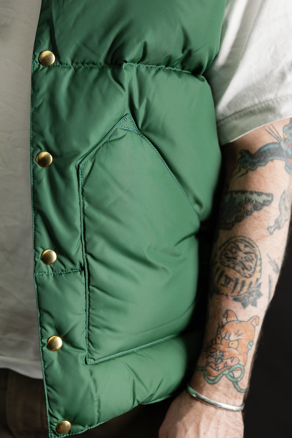 Close-up of front left side, bottle green nylon down vest, brass snaps, chest pocket; male model, 5'9