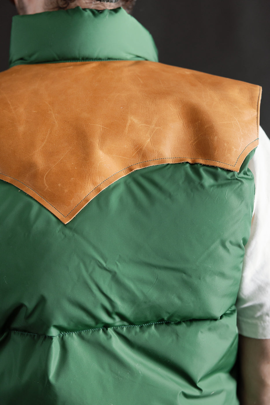 Close-up of male model's back wearing green nylon down vest with tan leather yoke, Dant apparel