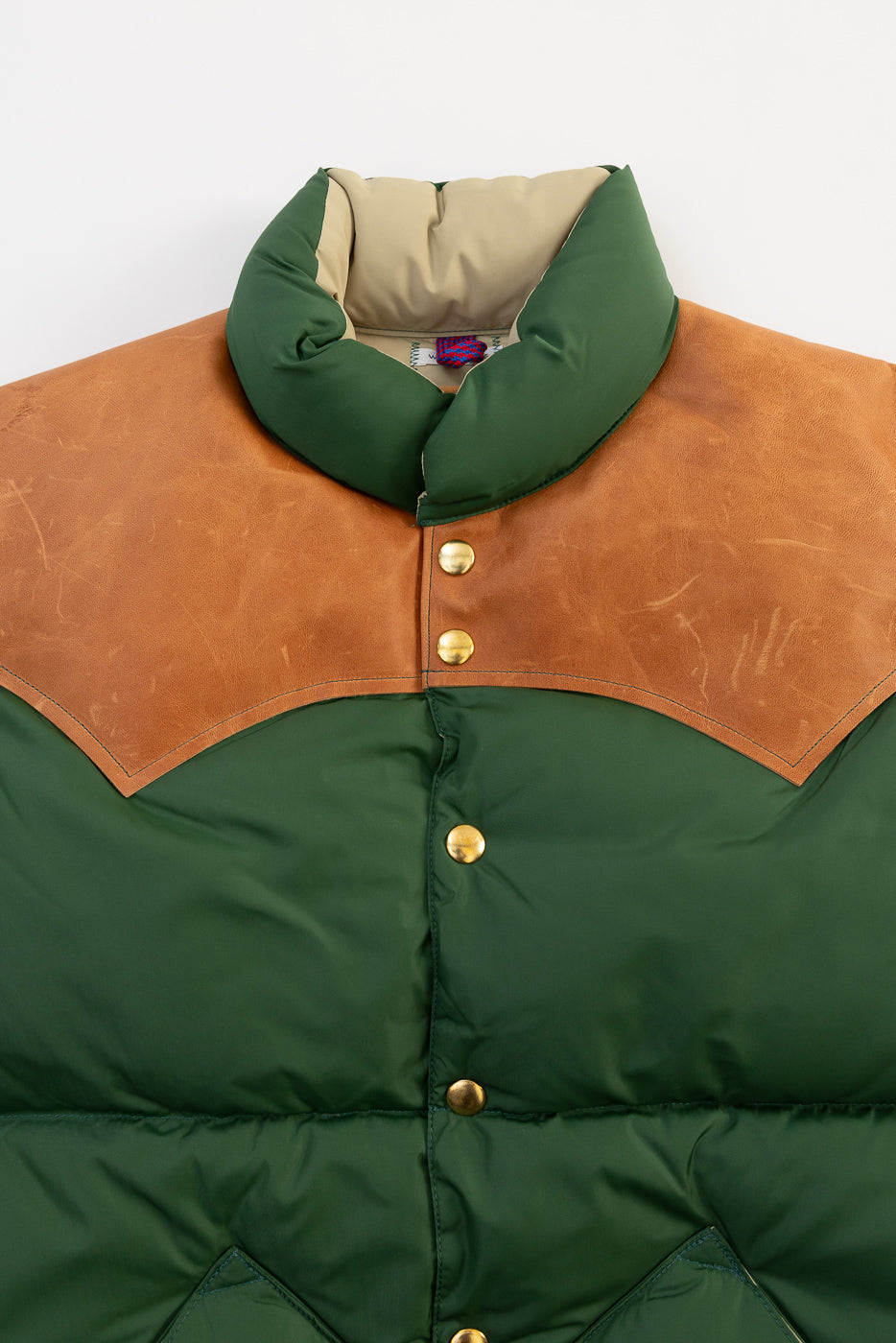 Close-up front view of bottle green nylon down vest, brown yoke, gold snap buttons, collar detail.