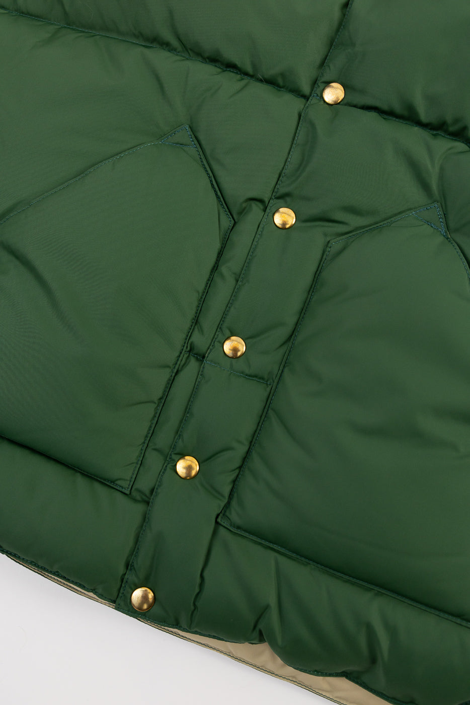 Close-up of Rocky Mountain green nylon down vest front with gold snap buttons and angled pockets.