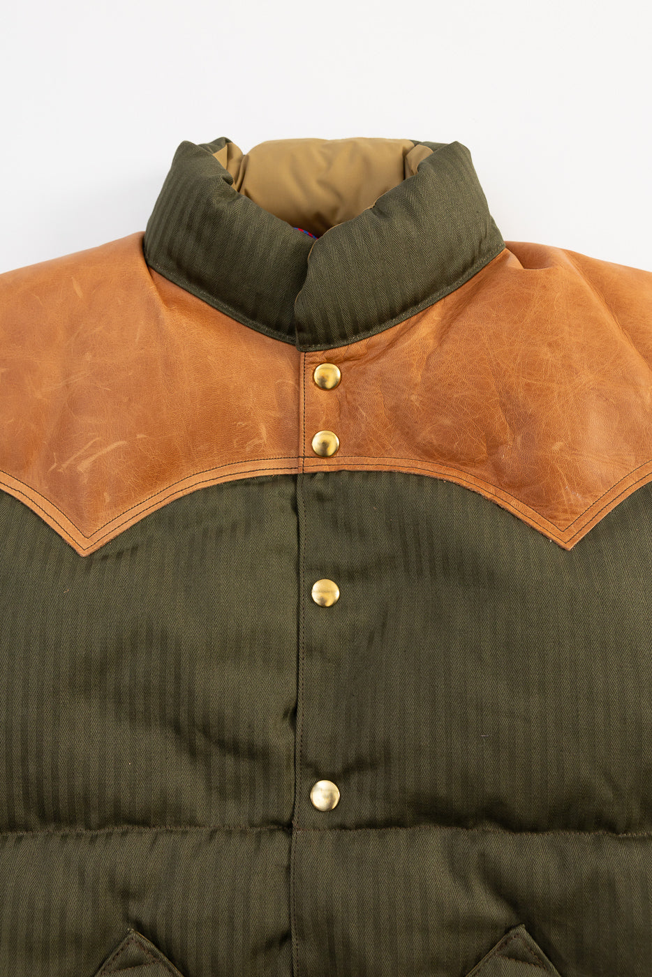 Close-up of Rocky Mountain Warehouse HBT down vest front, OD green with tan leather yoke, snap buttons, collar detail.