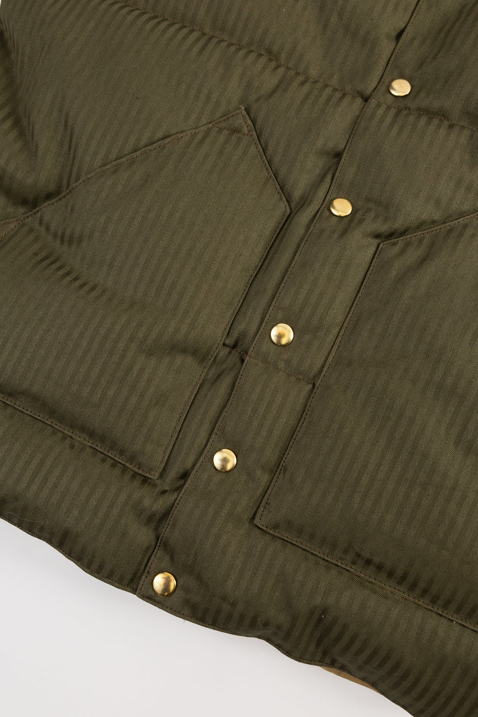 Close-up of Rocky Mountain HBT down vest in olive drab, front bottom, showing snap buttons and textured herringbone fabric at Dant.