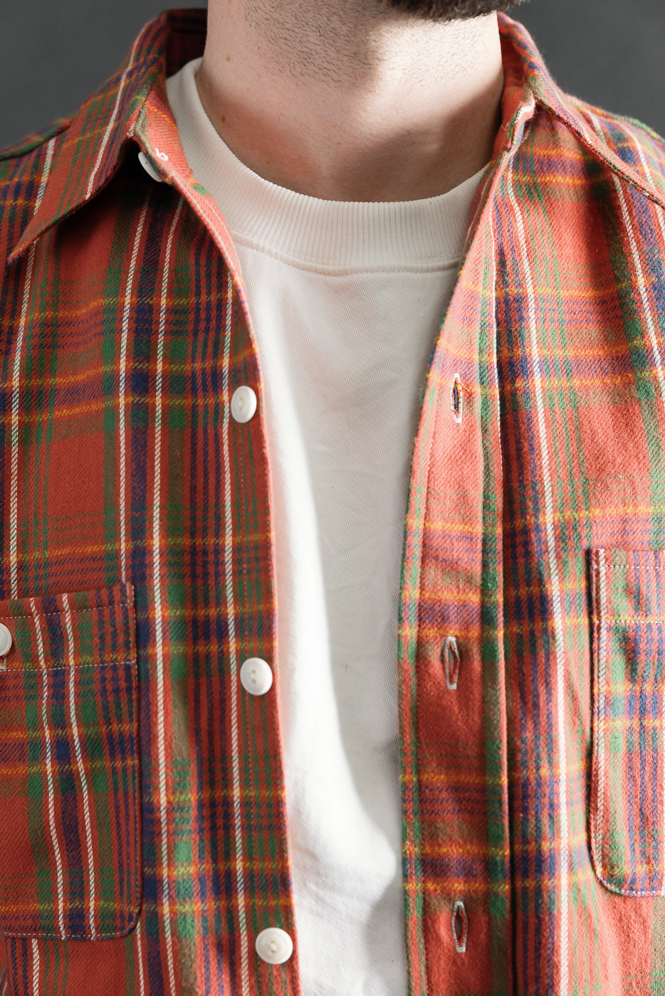 Close-up front view of red plaid storm shirt on male model, showing collar, chest pockets, and fabric texture. Model is 5'9